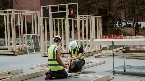 Workers in safety gear assembling wooden frames on a construction site outdoors.